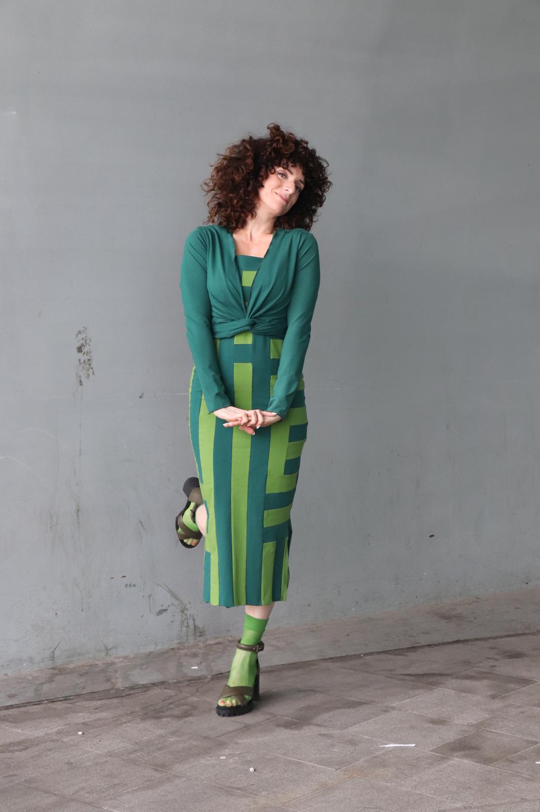 Vrouw draagt een handgemaakt groen wikkelvest van CLAU-D op een gestreepte jurk